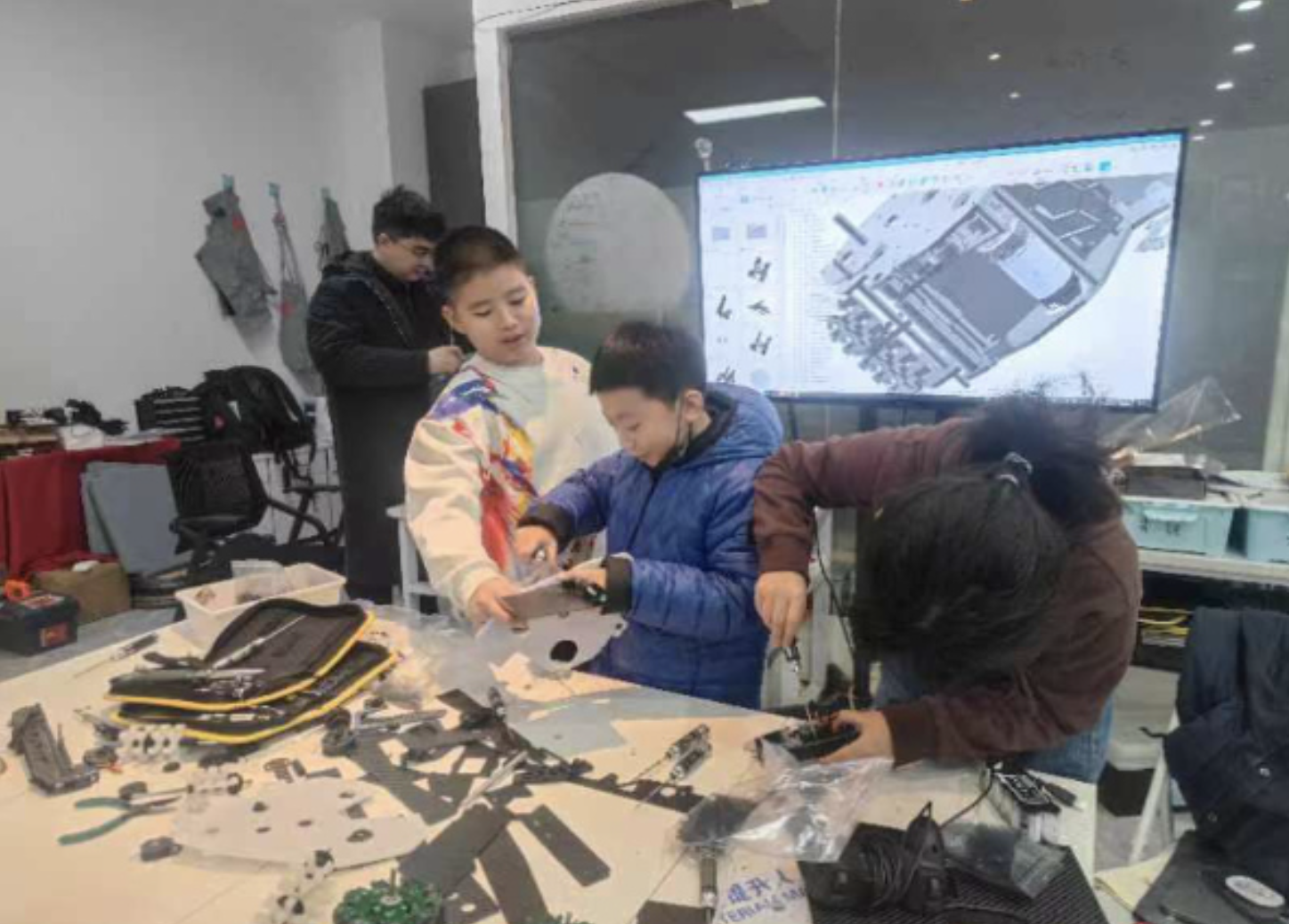 A group  of teenagers building a FTC robot with a TV showing the CAD at the back